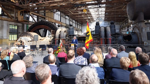 In der Gebläsehallte des ehemaligen Hüttenwerks Henrichshütte in Hattingen stehen große Maschinen, davor Bundespräsident Steinmeier, im Publikum sitzen zahlreiche Menschen