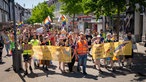 Beim ersten CSD in Hattingen laufen demonstrierende Menschen mit bunden Regenbogenfagen. Hattingen hat queeres Leben steht auf einem Plakat.