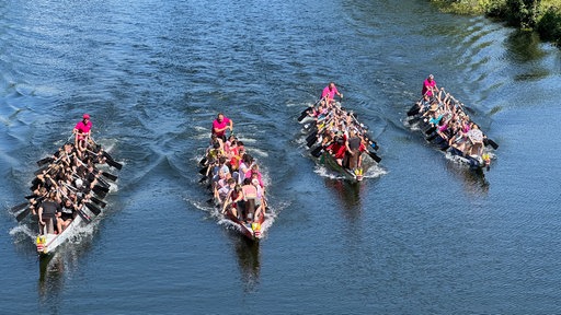 Vier Drachenboote sind auf einem Fluss und die Mannschaften rudern um die Wette. 