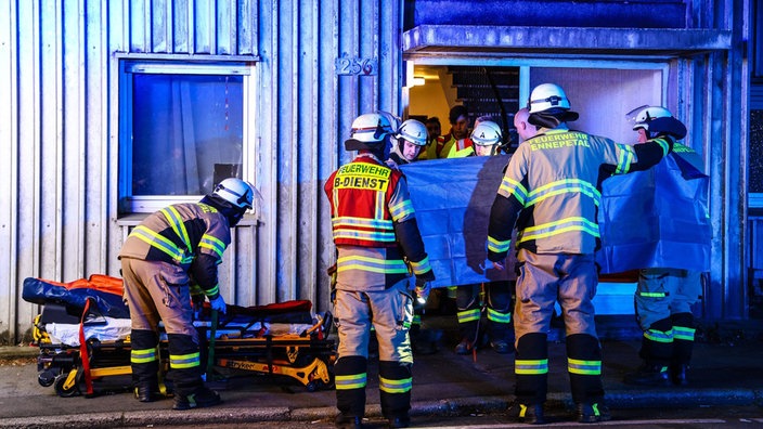 Rettungskräfte bilden mit einer Plane einen Sichtschutz aus dem Fenster gestürzten Mann.