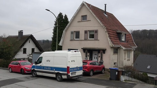 Ein beiges Einfamilienhaus, davor stehen zwei rote Autos und ein weißer Wagen mit der Aufschrift "KTU" und "Polizei".
