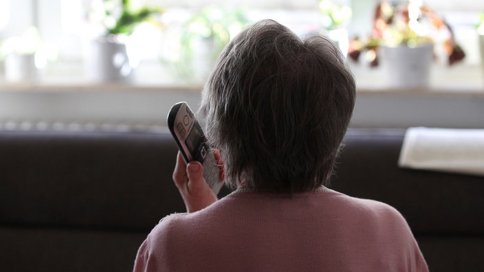 Eine ältere Dame ist von hinten zu sehen. Sie hält ein Telefon in der Hand.