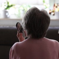 Eine ältere Dame ist von hinten zu sehen. Sie hält ein Telefon in der Hand.