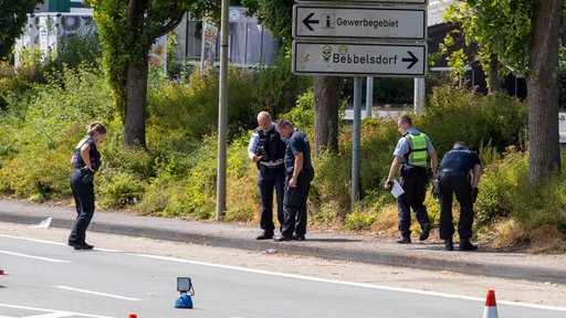 Fünf Polizisten stehen auf einer Straße und einem Bürgersteig und schauen sich einen Gegenstand an
