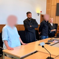 Die Angeklagten stehen neben Verteidiger und Verteidigerin im Gerichtssaal.