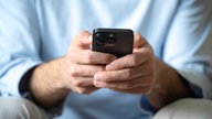 Symbolbild: Ein Mann hält ein Handy in der Hand, sein Gesicht ist nicht zu sehen. 