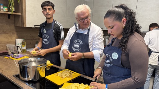 Bundespräsident Steinmeier steht mit zwei Jugendlichen in Küche und schneidet Kartoffeln