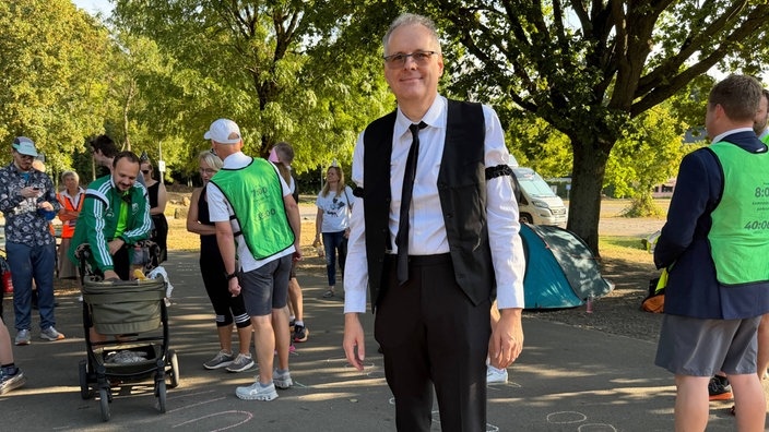 Veranstalter Arnd Bernstein, ein Mann in Weste und Krawatte, steht zwischen mehreren Läufern