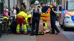 Einsatzkräfte behandeln eine Person, die auf dem Gehweg liegt.