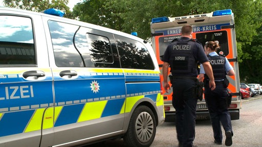 Polizisten stehen vor einem Krankenwagen.