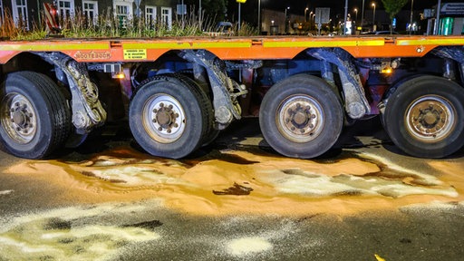 Mehrere Räder eines Schwertransporters nah, der Boden ist mit Bindemittel bedeckt. 