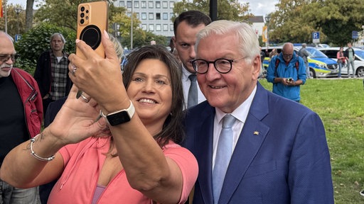 Frau macht mit Bundespräsident Steinmeier ein Selfie und hält ihr Handy in die Höhe