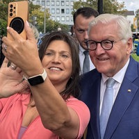 Frau macht mit Bundespräsident Steinmeier ein Selfie und hält ihr Handy in die Höhe
