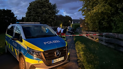 Ein Einsatzwagen der Polizei steht mit Rettungssanitätern am Tatort.