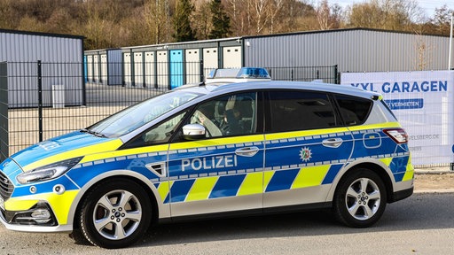Ein Einsatzwagen der Polizei steht vor dem eingezäunten Gelände eines Garagenhofs in Gevelsberg.