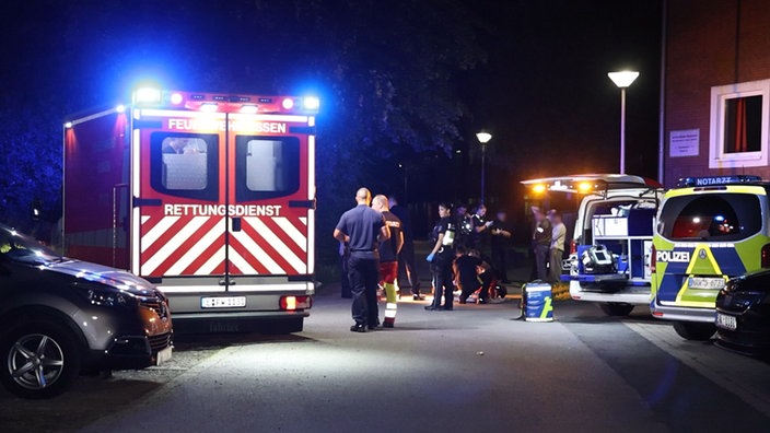 Einsatzkräfte stehen neben Rettungswagen und Polizeifahrzeugen am Tatort
