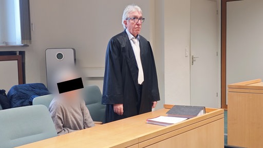 Die angeklagte Buchhalterin sitzt neben ihrem stehenden Verteidiger im Verhandlungsraum.