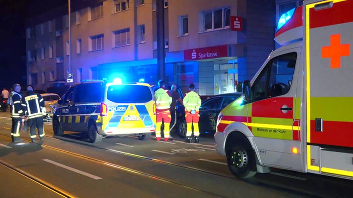 Eine Sparkassenfiliale im Hintergrund, davor sind Einsatzkräfte und Einsatzfahrzeuge mit Blaulicht zu sehen