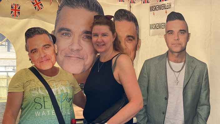 Eine Frau steht zwischen Pappaufstellern des Sängers Robbie Williams.