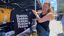 Eine Frau hält ein Fan-T-Shirt hoch.