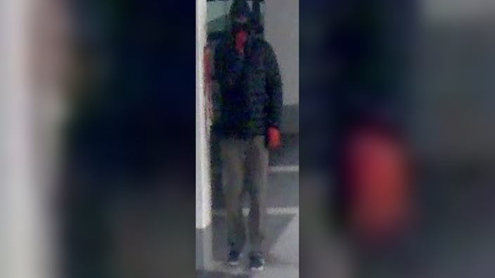 Ein dunkel gekleideter Mann mit Sturmhaube und roten Handschuhen steht in einem Parkhaus.