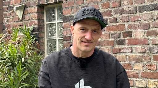 Daniel Cyris steht vor eine Backsteinmauer und schaut in die Kamera.