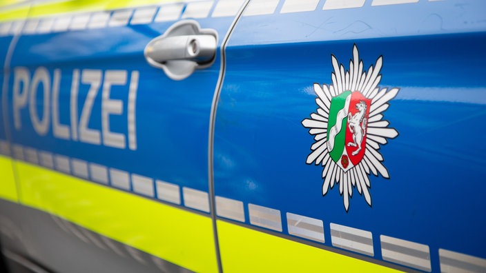 Auf der Seite eines Polizeiautos stehen das Wort "Polizei" und ein Wappen des Landes NRW