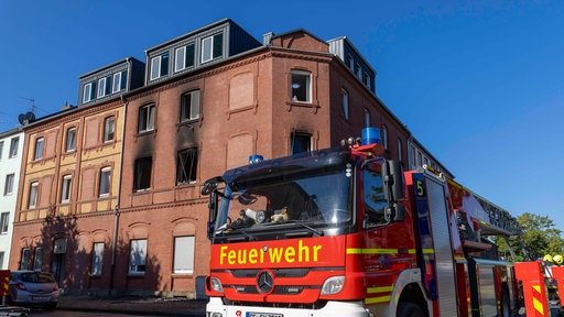 Brand in Gelsenkirchen: Vor einem ausgebrannten mehrstöckigen Backsteingebäude mit verrußten Fenstern steht ein Feuerwehrauto.