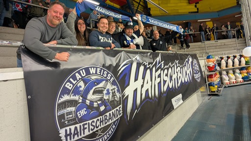 Sieben Männer und Frauen des Fanklubs "Haifischbande" stehen hinter einem Banner und halten Schals hoch.