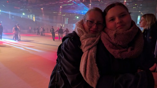 Michaela Lügger steht auf dem Eis und umarmt ihre Tochter, im Hintergrund sind Discolichter und andere Gäste auf dem Eis zu sehen
