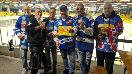 Sechs Männer stehen in alten Trikots der Schalker Haie in der Gelsenkirchener Eishalle und halten ihre Dauerkarte in die Kamera.