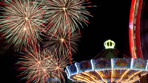 Ein bunt beleuchtetes Kettenkarussell auf der Cranger Kirmes, darüber leuchtendes Feuerwerk