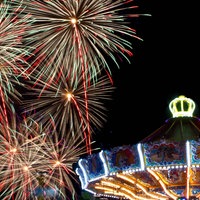 Ein bunt beleuchtetes Kettenkarussell auf der Cranger Kirmes, darüber leuchtendes Feuerwerk