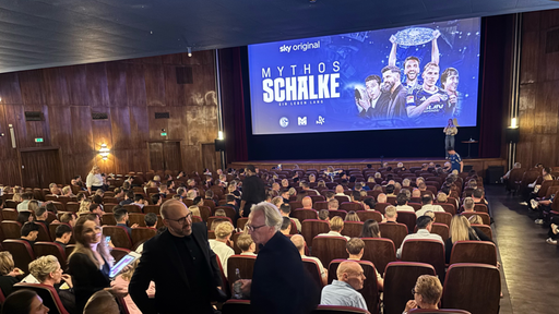 Ein gefüllter Kinosaal, helle Beleuchtung und eine Leinwand mit der Aufschrift "Mythos Schalke" im Hintergrund