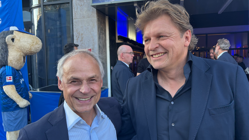 Olaf Thon und Youri Mulder stehen lächelnd vor dem Kinoeingang. 