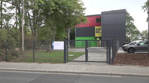 Blick auf das dreistöckige Grundschulgebäude, im Vordergrund eine Straße