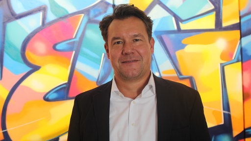 Marcel Hilgers steht vor einer bunten Wand.