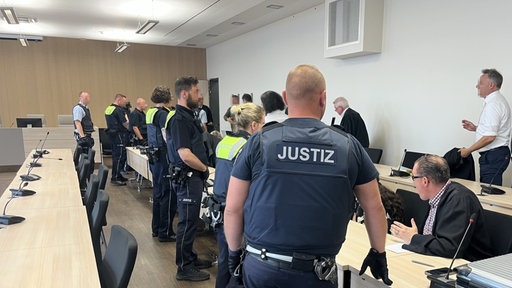Mehrere Menschen in einem Gerichtssaal, Mitarbeitende der Justiz, Rechtsanwälte und weitere Personen