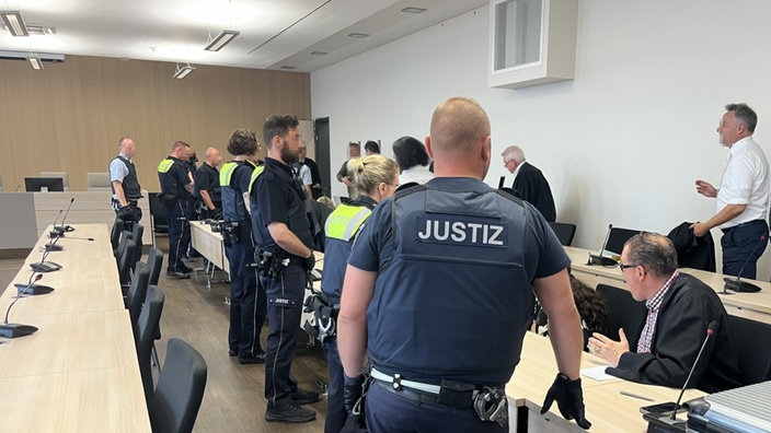 Mehrere Menschen in einem Gerichtssaal, Mitarbeitende der Justiz, Rechtsanwälte und weitere Personen