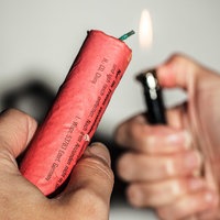 Eine Hand zündet mit einem Feuerzeug einen Böller in der anderen Hand an
