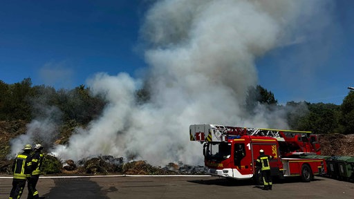 Ein Leiterwagen der Feuerwehr steht vor einem brennenden Grünschnitthaufen