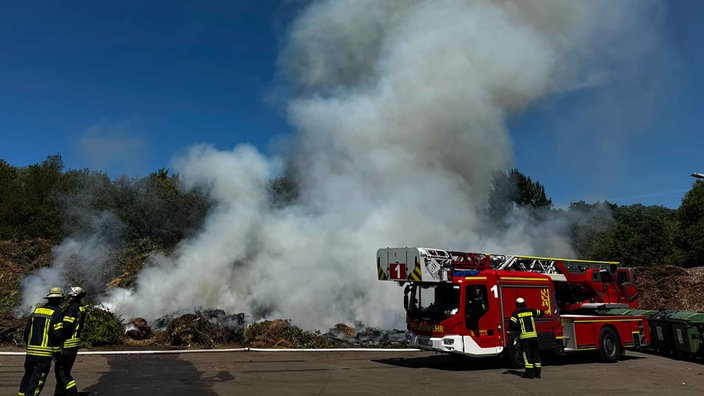 Ein Leiterwagen der Feuerwehr steht vor einem brennenden Grünschnitthaufen