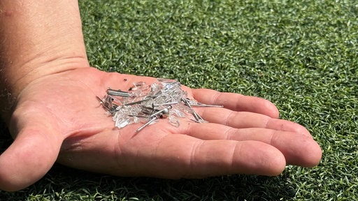 Eine Hand auf der mehrere kleine Glasscherben und Nägel liegen