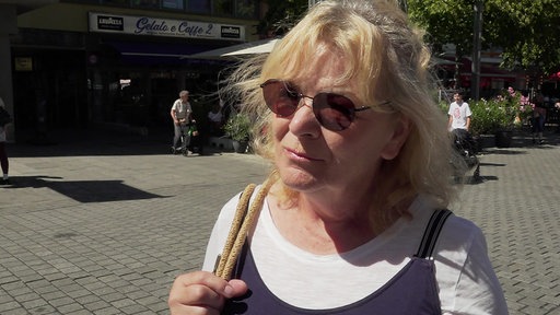 Frau mitblonden kurzen Haaren und Sonnenbrille steht in der Innenstadt.