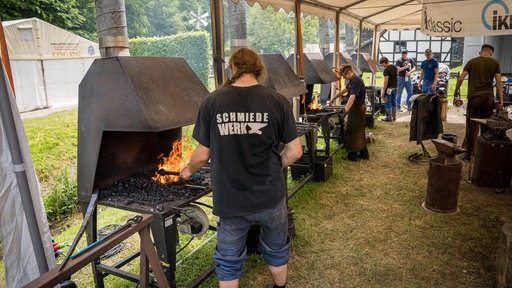Mehrere Schmiede stehen nebeneinander und arbeiten 