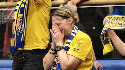 Eine Frau mit Trikot und Schal von Phoenix Hagen, die ihr Gesicht in den Händen vergräbt.