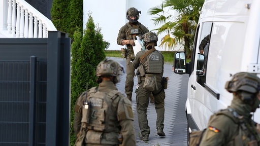 Einsatzkräfte der Polizei tragen Teile der gesprengten Haustür fort.
