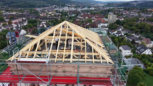 Ein Kirchendach von oben aufgenommen, man sieht Arbeiter und Dachbalken, die errichtet werden