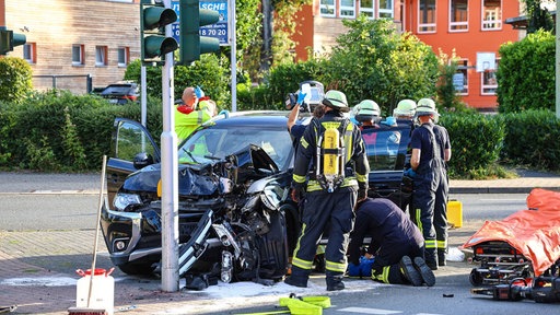 Ein schwarzer Pkw ist mit einer Ampel kollidiert. Drumherum stehen Einsatzkräfte.
