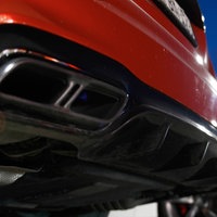Auf dem Foto ist das Heck eines roten Sportwagens, daneben steht ein weißer Audi.
